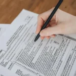 Tangan menulis di formulir dokumen pajak dengan pulpen hitam di atas meja kerja