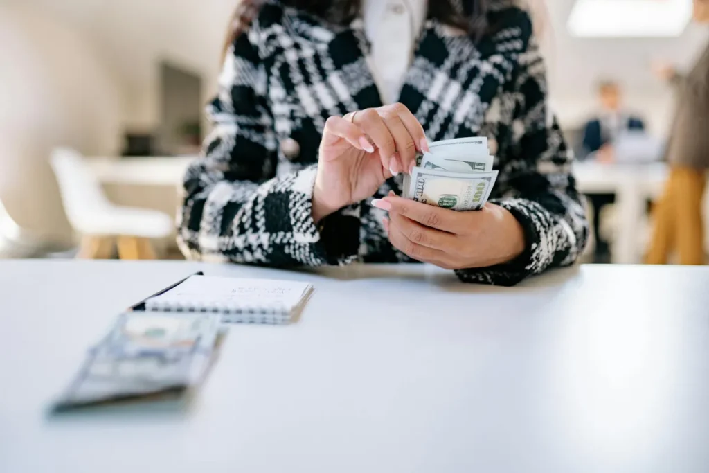 Karyawan menghitung uang tunai di lingkungan kantor, menggambarkan proses perhitungan gaji bersih atau take home pay